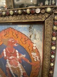 A Tibetan thangka in inlaid gilt brass frame, 19th C.